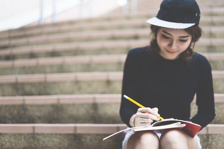 Smiling college student sitting on staircase and studying with books