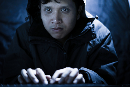 Hooded computer hacker stealing information with laptop