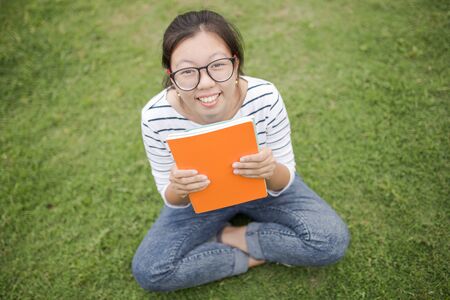 A female college student reading a book while lying on the parkの写真素材