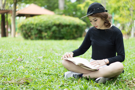 A female college student reading a book while lying on the parkの写真素材