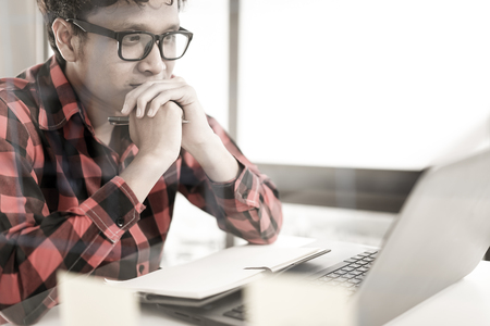 A young hispanic man working on a wooden desk with a laptop.の写真素材