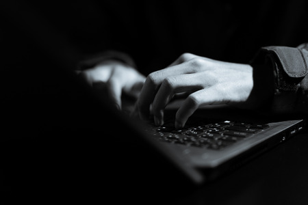 Hooded computer hacker stealing information with laptop