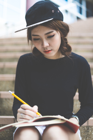 Smiling college student sitting on staircase and studying with booksの写真素材