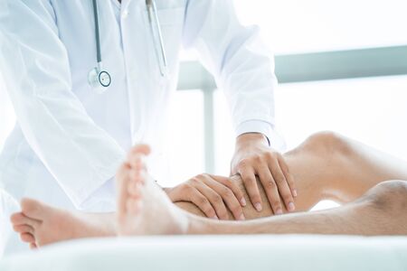 Close-up of male physiotherapist massaging the leg of patient in a physio room.の写真素材