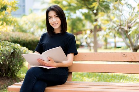 A female college student reading a book while lying on the parkの写真素材