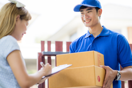 Asian woman receiving a package at home from a delivery guyの写真素材