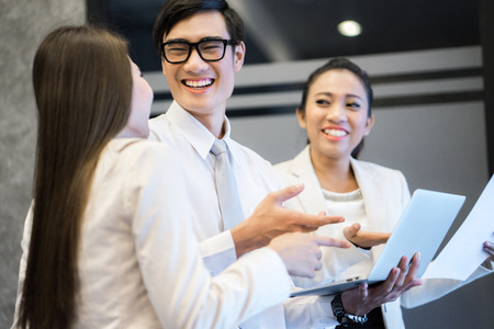 Three happy businesspeople standing in front of office, talking and smiling.の写真素材