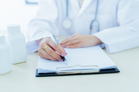 Close-up view of female doctor hands filling patient registration form. Healthcare and medical conceptの写真素材
