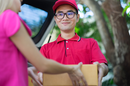 Asian woman receiving a package at home from a delivery guyの写真素材