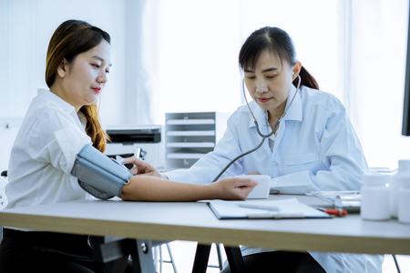 Doctor visiting a patient and checking her blood pressure at the hospitalの写真素材