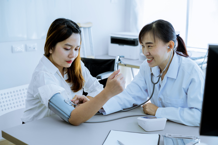 Doctor visiting a patient and checking her blood pressure at the hospitalの写真素材