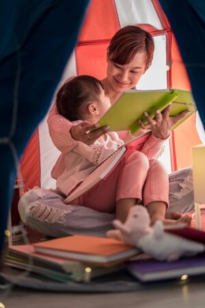 Asian mother and child daughter with book and flashlight before going to bedの写真素材