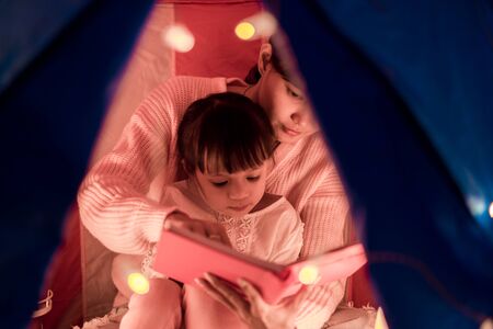 reading and family games in children's tent. asian mother and child daughter with book and flashlight before going to bedの写真素材