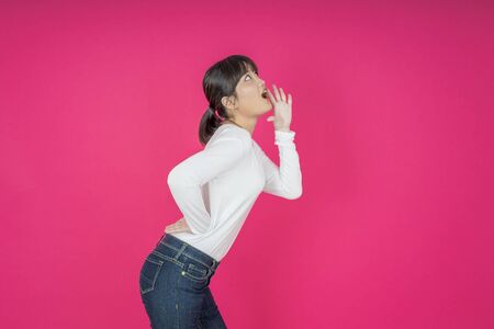 Do not miss. Young asian woman shouting. Shout. Crying emotional  woman screaming on pink studio background. Female half-length portrait. Human emotions, facial expression concept. Trendyの写真素材