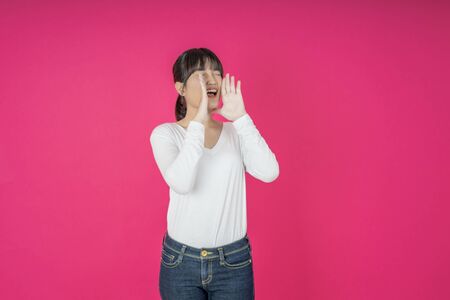 Do not miss. Young asian woman shouting. Shout. Crying emotional  woman screaming on pink studio background. Female half-length portrait. Human emotions, facial expression concept. Trendyの写真素材