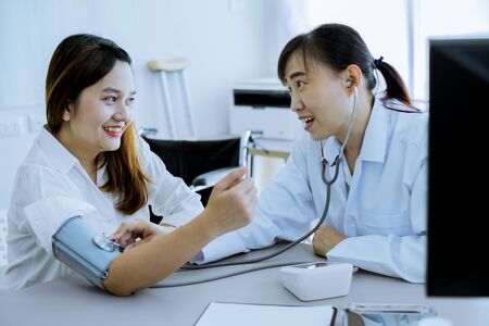 Doctor visiting a patient and checking her blood pressure at the hospitalの写真素材
