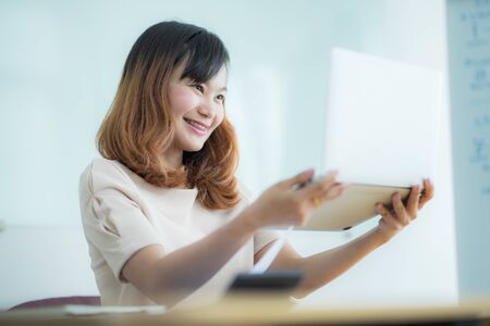 Asian businesswoman laughing with joy at workplace, gladly looking at laptop screen, feeling excited about online win, watching funny video on computer, enjoying positive good news in internetの写真素材