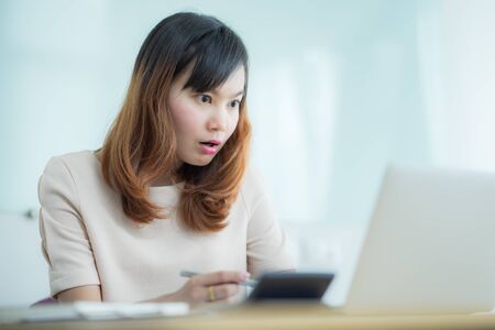 Asian businesswoman laughing with joy at workplace, gladly looking at laptop screen, feeling excited about online win, watching funny video on computer, enjoying positive good news in internetの写真素材