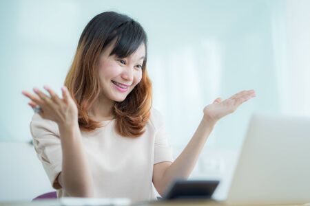 Asian businesswoman laughing with joy at workplace, gladly looking at laptop screen, feeling excited about online win, watching funny video on computer, enjoying positive good news in internetの写真素材