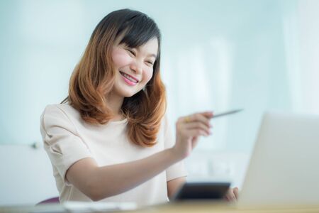 Asian businesswoman laughing with joy at workplace, gladly looking at laptop screen, feeling excited about online win, watching funny video on computer, enjoying positive good news in internetの写真素材