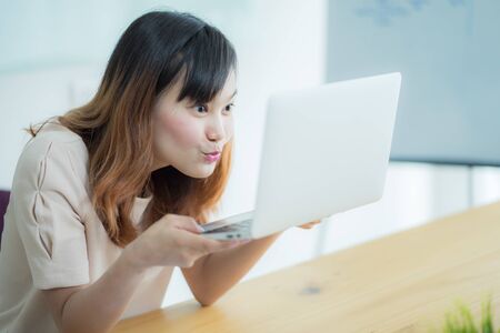 Asian businesswoman laughing with joy at workplace, gladly looking at laptop screen, feeling excited about online win, watching funny video on computer, enjoying positive good news in internetの写真素材