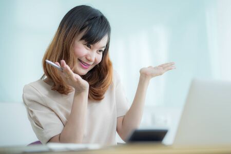 Asian businesswoman laughing with joy at workplace, gladly looking at laptop screen, feeling excited about online win, watching funny video on computerの写真素材