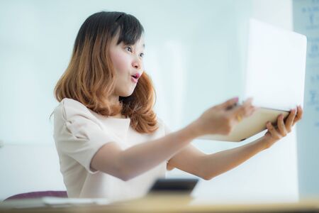 Asian businesswoman laughing with joy at workplace, gladly looking at laptop screen, feeling excited about online win, watching funny video on computer, enjoying positive good news in internetの写真素材