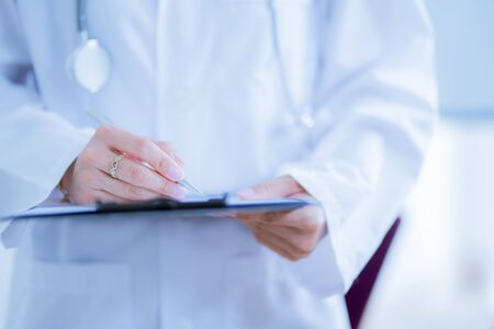 Close-up view of female doctor hands filling patient registration form. Healthcare and medical conceptの写真素材