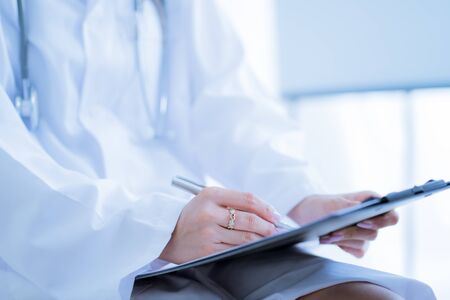 Close-up view of female doctor hands filling patient registration form. Healthcare and medical conceptの写真素材