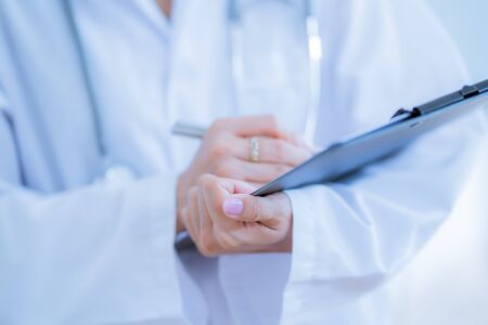Close-up view of female doctor hands filling patient registration form. Healthcare and medical conceptの写真素材