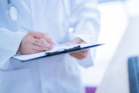 Close-up view of female doctor hands filling patient registration form. Healthcare and medical conceptの写真素材