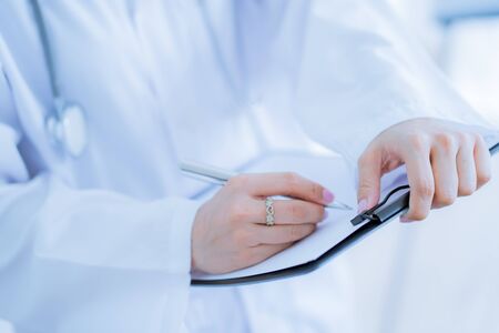 Close-up view of female doctor hands filling patient registration form. Healthcare and medical conceptの写真素材