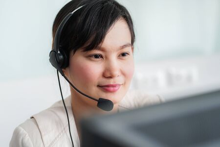 Portrait of happy smiling female customer support phone operator at workplace. Asianの写真素材