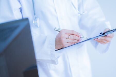 Close-up view of female doctor hands filling patient registration form. Healthcare and medical conceptの写真素材