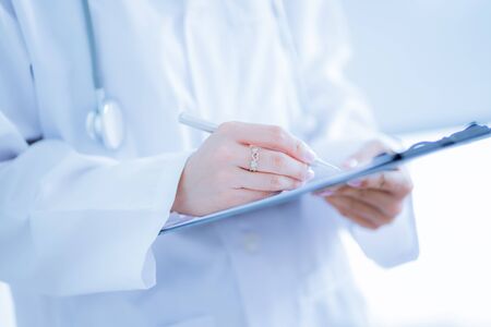 Close-up view of female doctor hands filling patient registration form. Healthcare and medical conceptの写真素材
