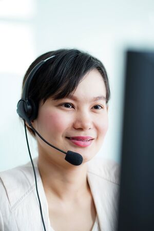 Portrait of happy smiling female customer support phone operator at workplace. Asianの写真素材