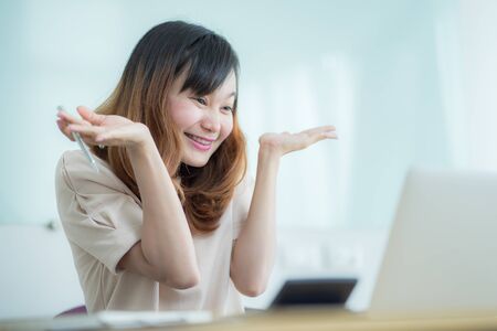 Asian businesswoman laughing with joy at workplace, gladly looking at laptop screen, feeling excited about online win, watching funny video on computer, enjoying positive good news in internetの写真素材