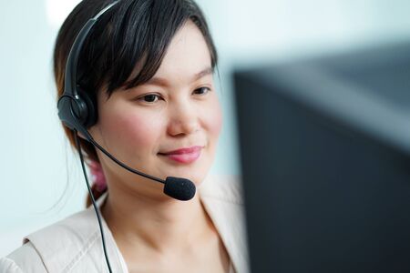 Portrait of happy smiling female customer support phone operator at workplace. Asianの写真素材