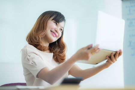 Asian businesswoman laughing with joy at workplace, gladly looking at laptop screen, feeling excited about online win, watching funny video on computer, enjoying positive good news in internetの写真素材