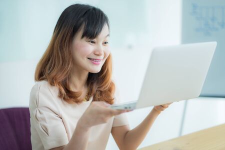 Asian businesswoman laughing with joy at workplace, gladly looking at laptop screen, feeling excited about online win, watching funny video on computer, enjoying positive good news in internetの写真素材