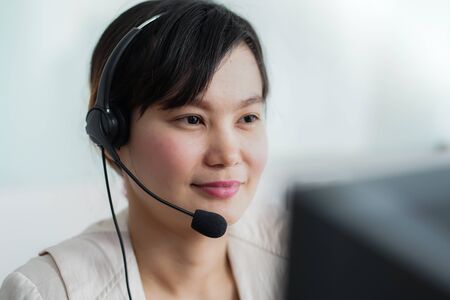 Portrait of happy smiling female customer support phone operator at workplace. Asianの写真素材