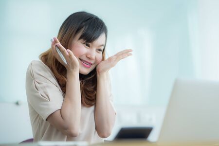Asian businesswoman laughing with joy at workplace, gladly looking at laptop screen, feeling excited about online win, watching funny video on computer, enjoying positive good news in internetの写真素材