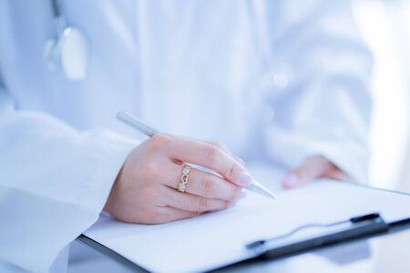 Close-up view of female doctor hands filling patient registration form. Healthcare and medical conceptの写真素材