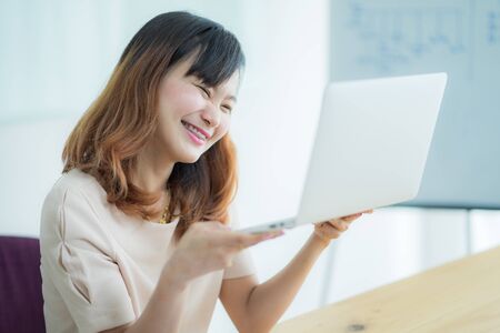 Asian businesswoman laughing with joy at workplace, gladly looking at laptop screen, feeling excited about online win, watching funny video on computer, enjoying positive good news in internetの写真素材