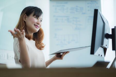 Asian businesswoman laughing with joy at workplace, gladly looking at laptop screen, feeling excited about online win, watching funny video on computer, enjoying positive good news in internetの写真素材