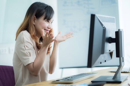 Asian businesswoman laughing with joy at workplace, gladly looking at laptop screen, feeling excited about online win, watching funny video on computer, enjoying positive good news in internetの写真素材