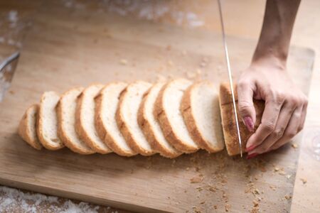 Fresh bread on the kitchen table The healthy eating and traditional bakery concept. Whole grain bread put on kitchen wood plate with a chef holding gold knife for cut. Fresh bread on table close-upの写真素材