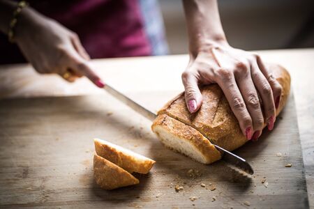 Fresh bread on the kitchen table The healthy eating and traditional bakery concept. Whole grain bread put on kitchen wood plate with a chef holding gold knife for cut. Fresh bread on table close-upの写真素材