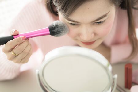 Asian woman looking to mirror doing makeup at homeの写真素材