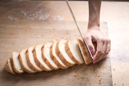 Fresh bread on the kitchen table The healthy eating and traditional bakery concept. Whole grain bread put on kitchen wood plate with a chef holding gold knife for cut. Fresh bread on table close-upの写真素材